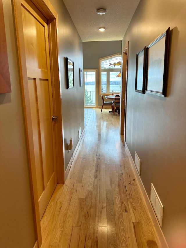 hall featuring baseboards, visible vents, light wood-style flooring, and a textured ceiling