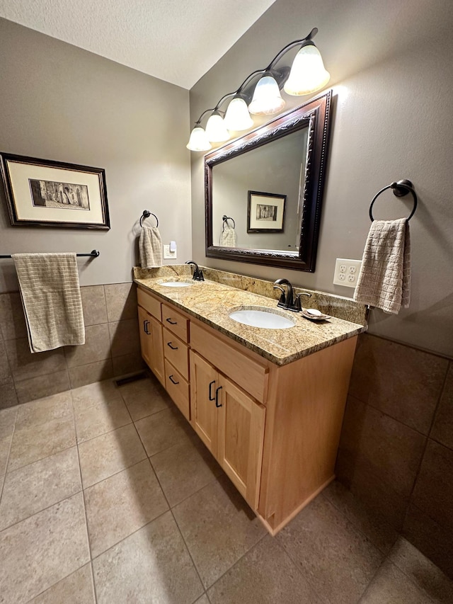 bathroom with a textured ceiling, double vanity, tile patterned flooring, and a sink