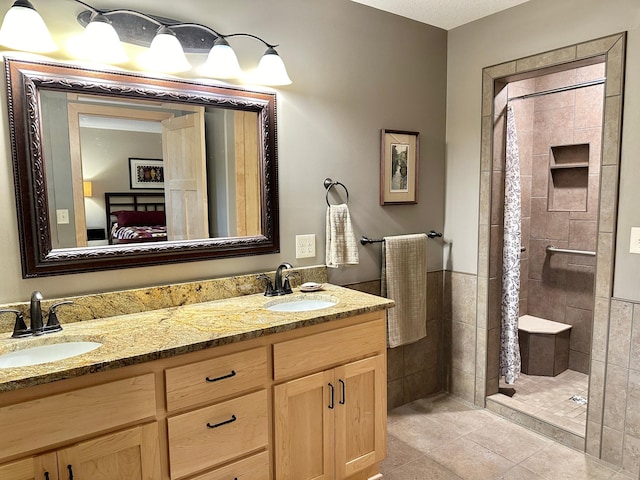 ensuite bathroom with a tile shower, tile patterned floors, a sink, and connected bathroom