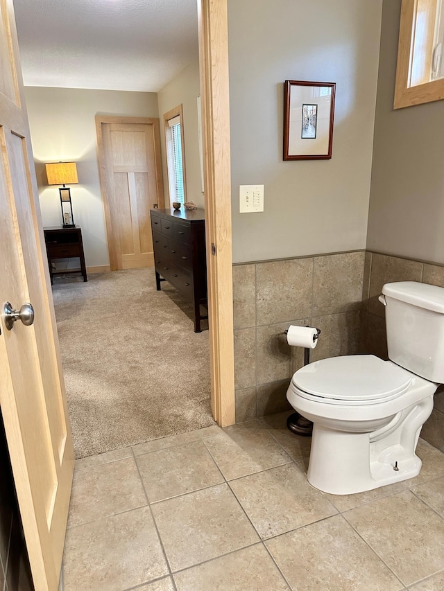 half bathroom with toilet, a wainscoted wall, tile patterned flooring, and tile walls