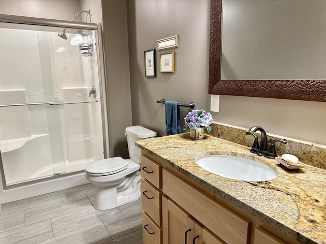 bathroom featuring a stall shower, wood finish floors, vanity, and toilet