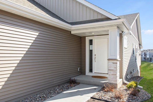 doorway to property featuring board and batten siding and roof with shingles