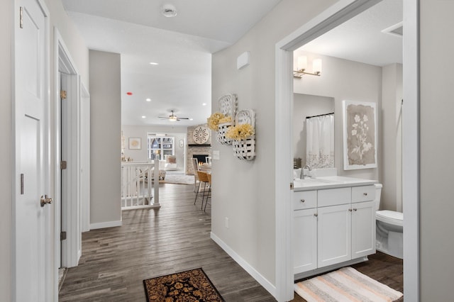 hallway featuring recessed lighting, baseboards, dark wood-style flooring, and a sink