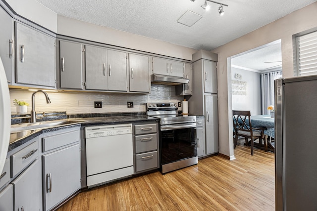 kitchen with dark countertops, gray cabinets, appliances with stainless steel finishes, a sink, and under cabinet range hood