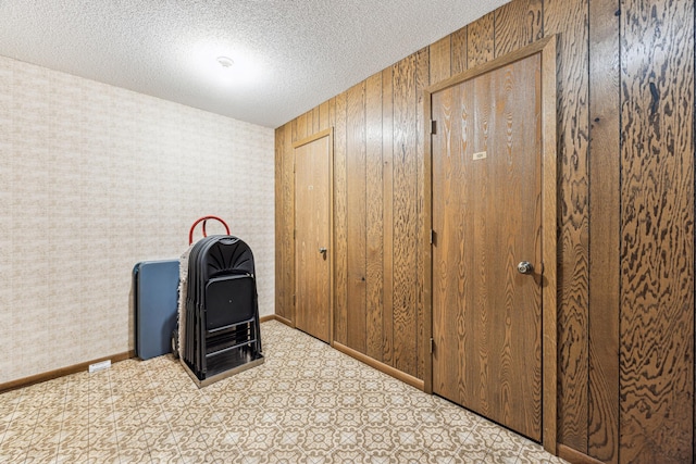 interior space featuring a textured ceiling, baseboards, and wallpapered walls