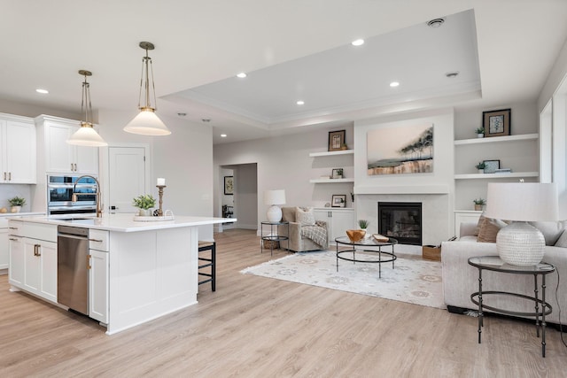 kitchen featuring a kitchen island with sink, a tray ceiling, white cabinets, and appliances with stainless steel finishes