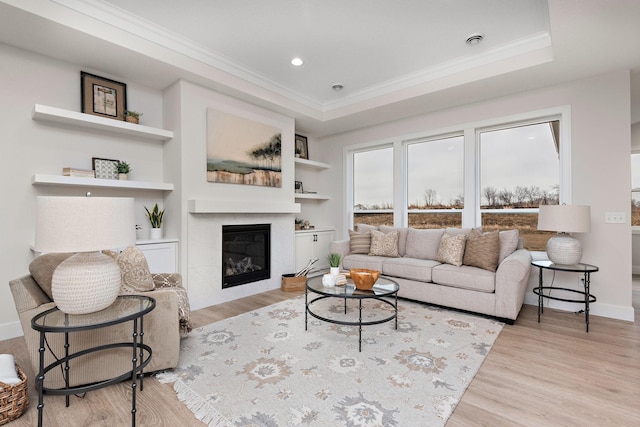 living area featuring built in features, a glass covered fireplace, crown molding, and wood finished floors