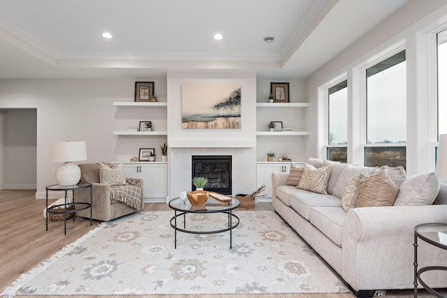 living area with a raised ceiling, ornamental molding, wood finished floors, built in shelves, and a high end fireplace