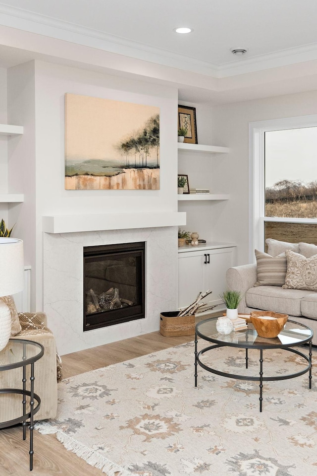 living room with built in features, wood finished floors, a high end fireplace, and crown molding