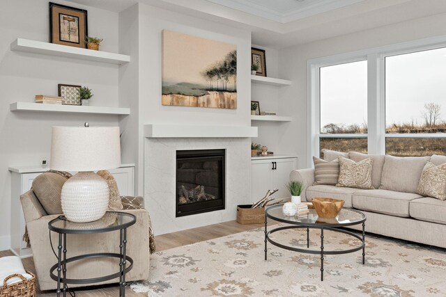 living area with built in features, wood finished floors, ornamental molding, and a premium fireplace