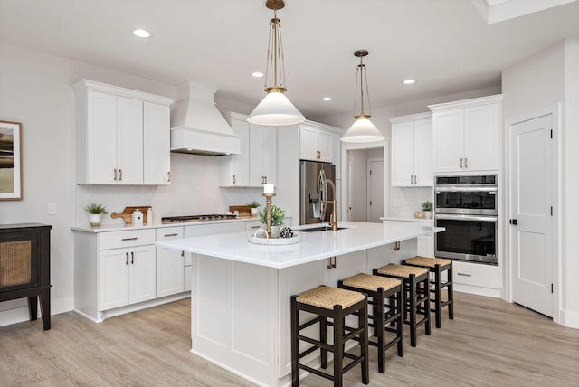 kitchen featuring light wood finished floors, premium range hood, appliances with stainless steel finishes, and a kitchen breakfast bar