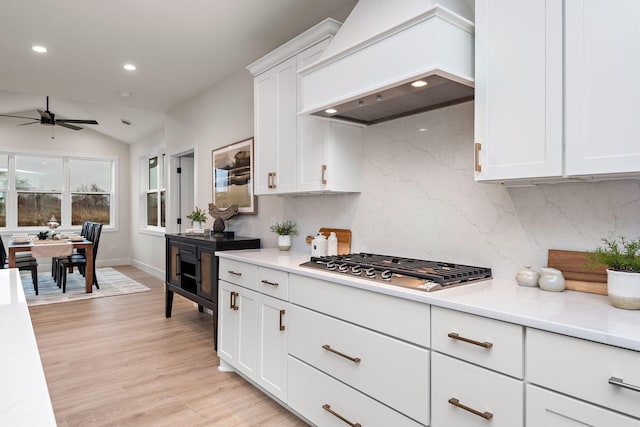 kitchen with light wood finished floors, tasteful backsplash, custom exhaust hood, light countertops, and stainless steel gas cooktop