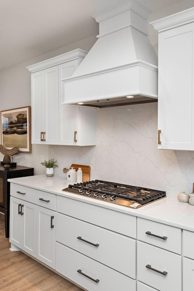 kitchen featuring stainless steel gas cooktop, custom exhaust hood, light countertops, and decorative backsplash