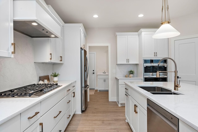 kitchen with stainless steel appliances, white cabinets, premium range hood, and a sink