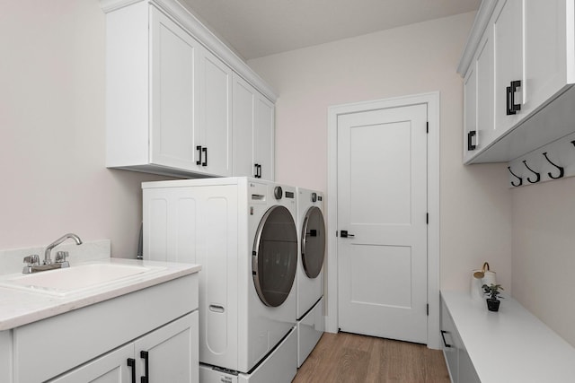 clothes washing area with cabinet space, light wood-style flooring, washer and dryer, and a sink