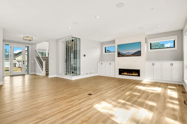 unfurnished living room featuring a large fireplace, visible vents, baseboards, stairs, and light wood-style floors