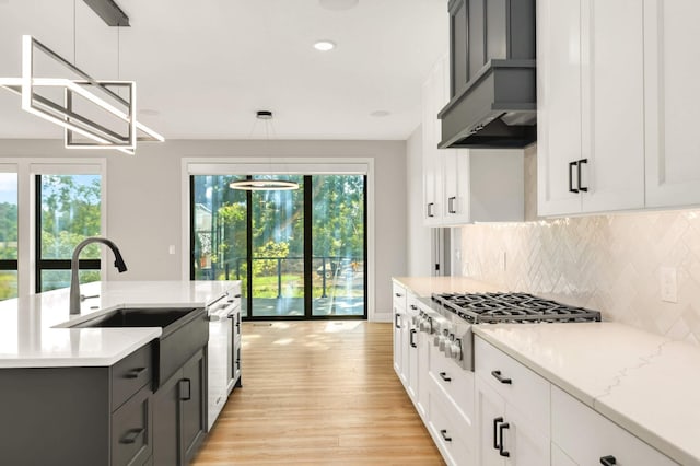 kitchen featuring light wood-style flooring, stainless steel gas cooktop, a sink, wall chimney exhaust hood, and tasteful backsplash