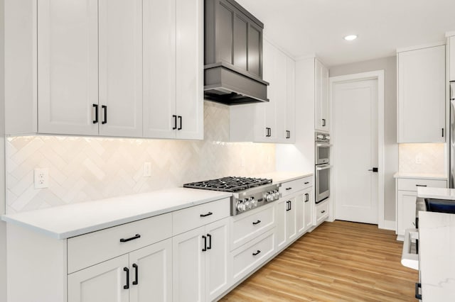 kitchen with light wood-style flooring, appliances with stainless steel finishes, custom exhaust hood, light countertops, and white cabinetry