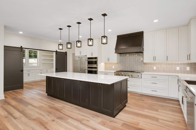 kitchen with light countertops, custom range hood, light wood-style flooring, a barn door, and appliances with stainless steel finishes