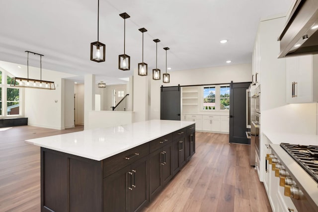 kitchen with light countertops, a barn door, wall chimney range hood, and a center island