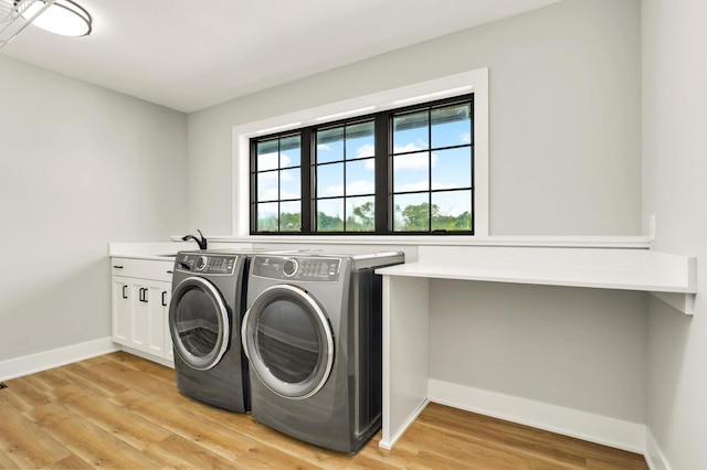 clothes washing area with cabinet space, light wood finished floors, baseboards, washing machine and dryer, and a sink