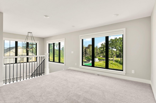 carpeted empty room featuring a chandelier, visible vents, a wealth of natural light, and baseboards