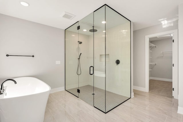 full bath featuring a spacious closet, a stall shower, a freestanding tub, and baseboards