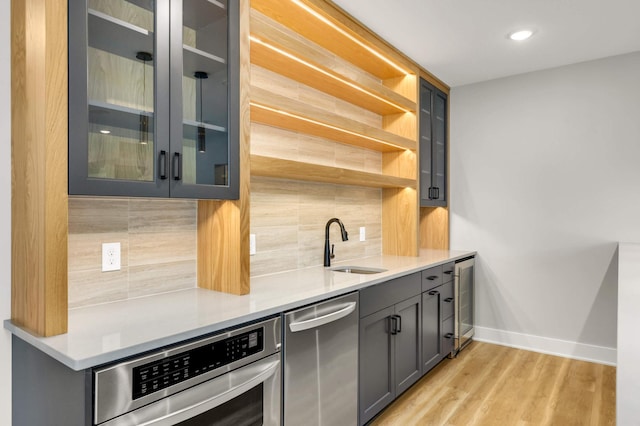 bar with a sink, baseboards, appliances with stainless steel finishes, light wood-type flooring, and decorative backsplash