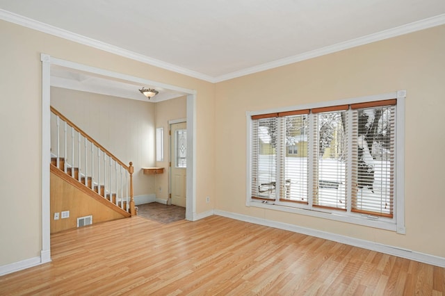 spare room featuring wood finished floors, visible vents, baseboards, stairs, and ornamental molding