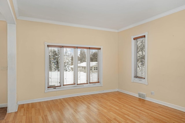 spare room featuring ornamental molding, light wood-type flooring, visible vents, and baseboards