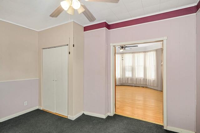 unfurnished bedroom with dark colored carpet, crown molding, baseboards, and ceiling fan