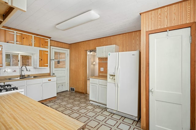 kitchen with white appliances, wooden walls, light countertops, light floors, and a sink