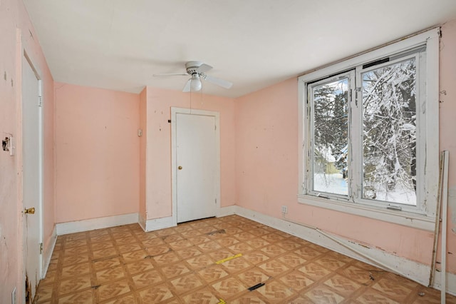 empty room featuring light floors, a ceiling fan, and baseboards