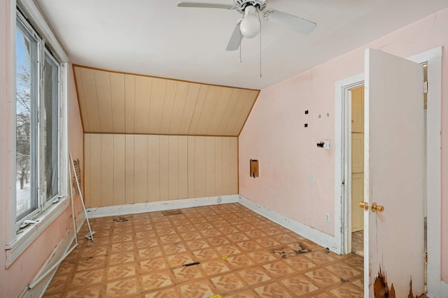 additional living space with wooden walls, baseboards, a ceiling fan, vaulted ceiling, and light floors