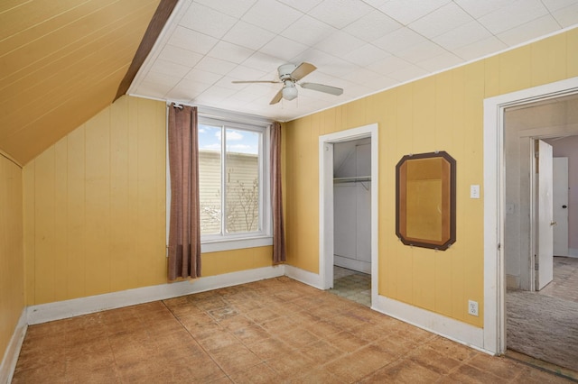 unfurnished bedroom with lofted ceiling, ceiling fan, wood walls, and a closet