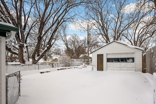 yard covered in snow with a garage, an outbuilding, and fence