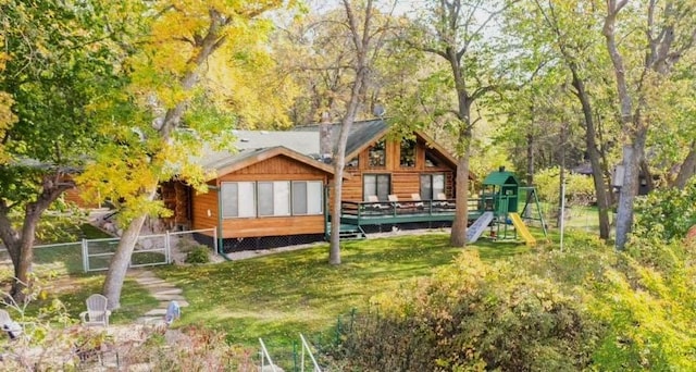 rear view of property featuring a playground, a yard, a deck, and fence