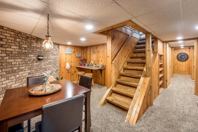 carpeted dining area featuring wooden walls, recessed lighting, a drop ceiling, and stairway