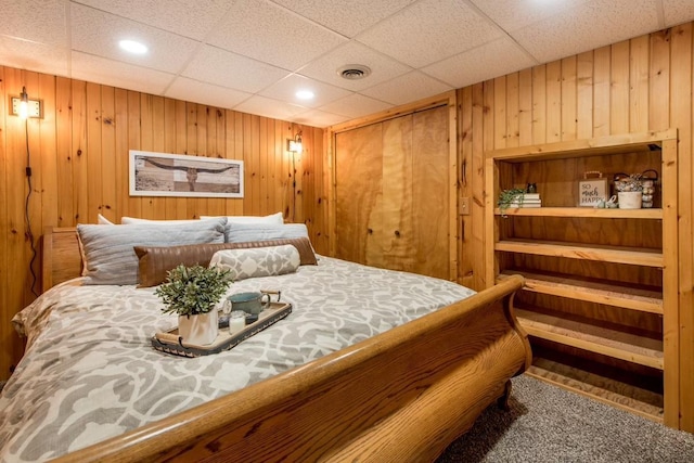 bedroom with wooden walls, visible vents, and a drop ceiling