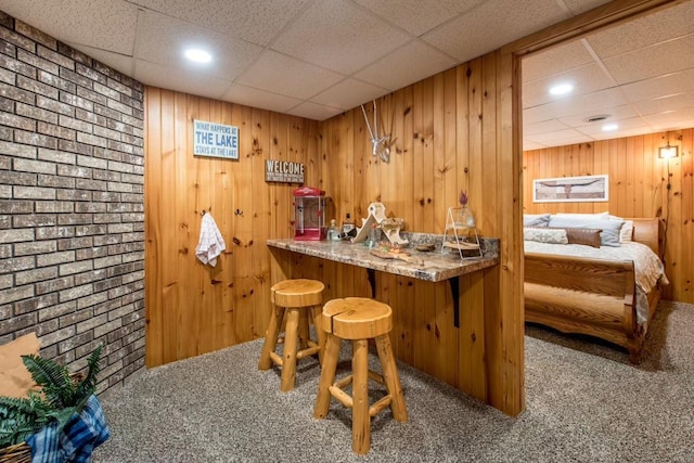 bar with carpet floors, wood walls, bar area, and a drop ceiling