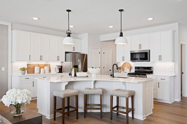 kitchen featuring a center island with sink, white cabinets, appliances with stainless steel finishes, a kitchen breakfast bar, and a sink