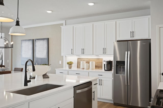 kitchen featuring stainless steel appliances, light countertops, hanging light fixtures, white cabinetry, and a sink