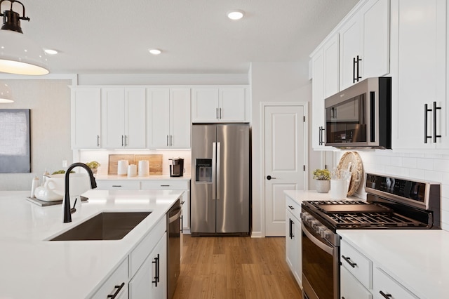 kitchen with stainless steel appliances, light countertops, white cabinetry, and a sink