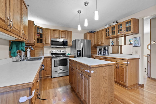 kitchen with light wood finished floors, a kitchen island, a sink, appliances with stainless steel finishes, and brown cabinets