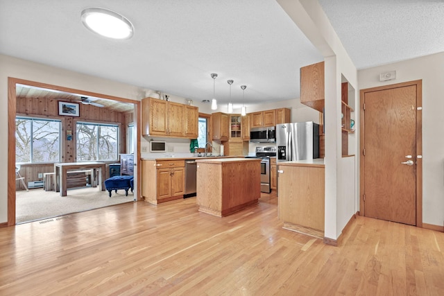 kitchen with a healthy amount of sunlight, light wood-style floors, appliances with stainless steel finishes, and a kitchen island