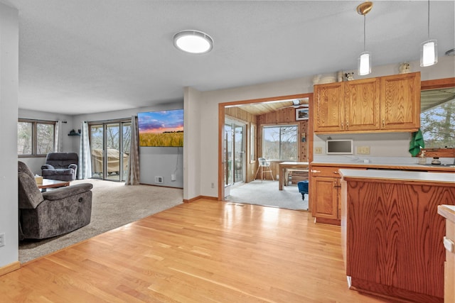 kitchen with baseboards, open floor plan, pendant lighting, light countertops, and light wood-style flooring