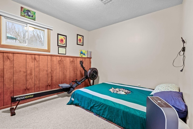 carpeted bedroom featuring wooden walls, wainscoting, and a textured ceiling