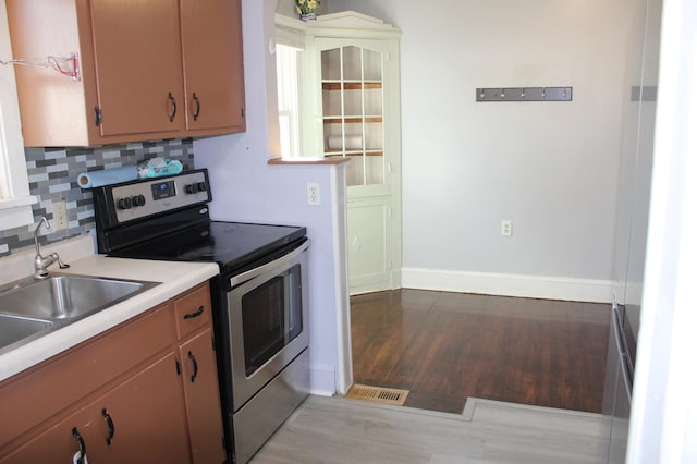 kitchen with light wood-style flooring, a sink, stainless steel range with electric cooktop, light countertops, and decorative backsplash