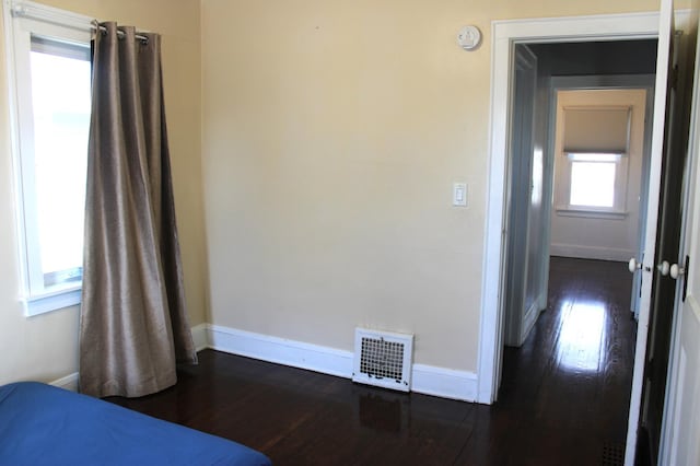 unfurnished bedroom with dark wood-style floors, visible vents, and baseboards