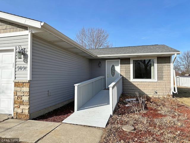 doorway to property with an attached garage, stone siding, and roof with shingles